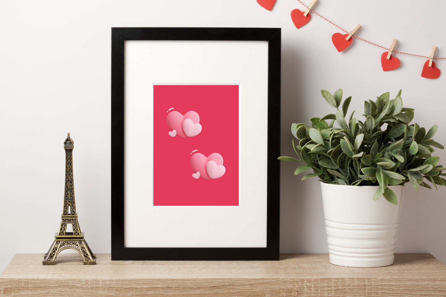 Framed artwork with pink hearts with a red background, placed on a wooden shelf with decorative items.