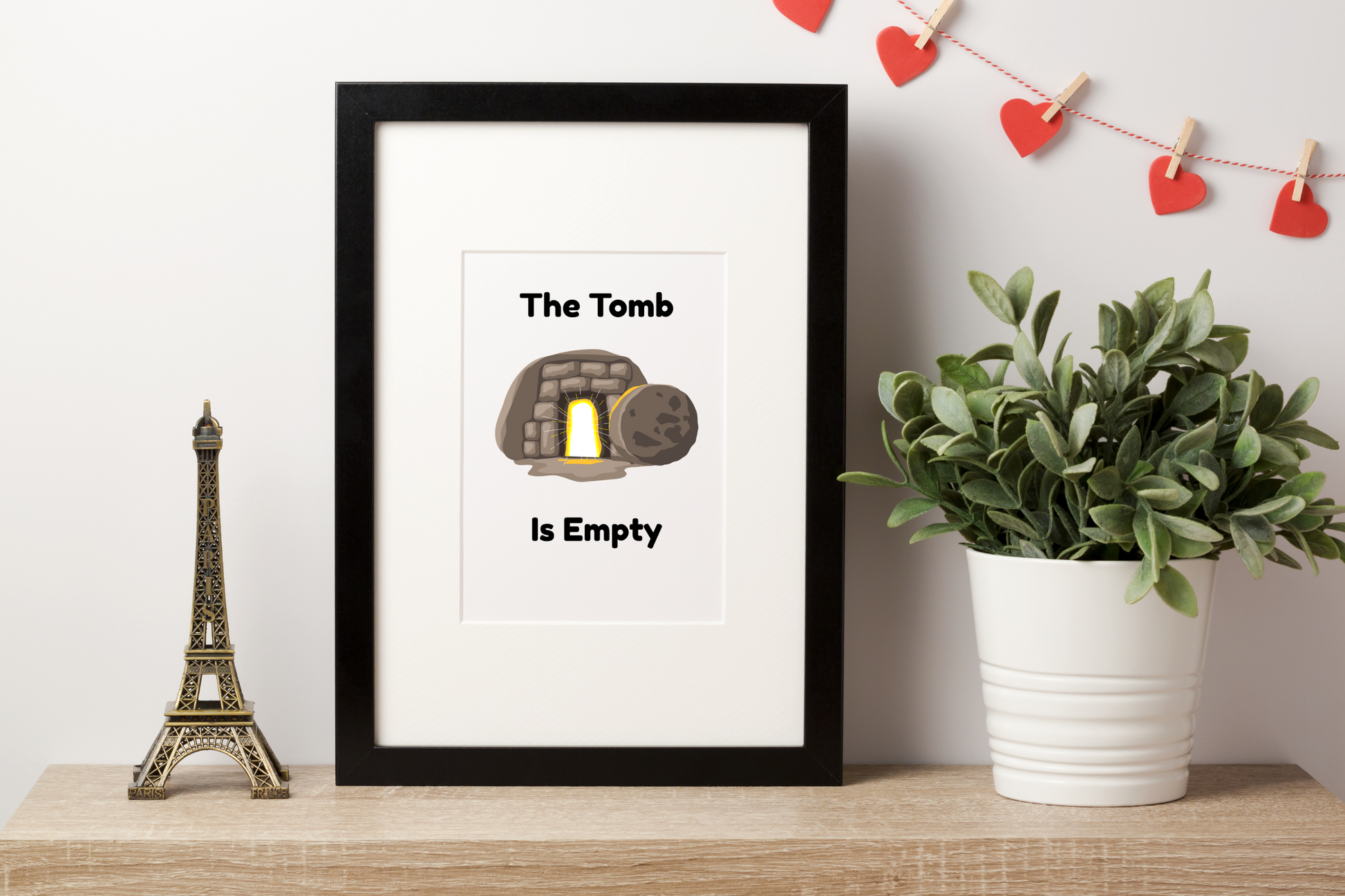 Framed artwork with 'The Tomb is Empty' text and illustration on a shelf with decorative items.