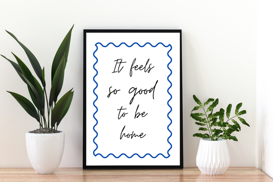 High-definition cobalt blue quote print "It feels so good to be home" framed in a clean and modern hallway space, perfect for uplifting everyday décor.