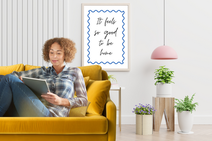 Inspirational cobalt blue printable wall art with "It feels so good to be home" quote, styled in a minimalist living room with neutral tones and clean aesthetic décor.