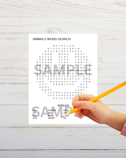 Child's hand holding a pencil over an 'Animals Word Search' sheet on a wooden surface.