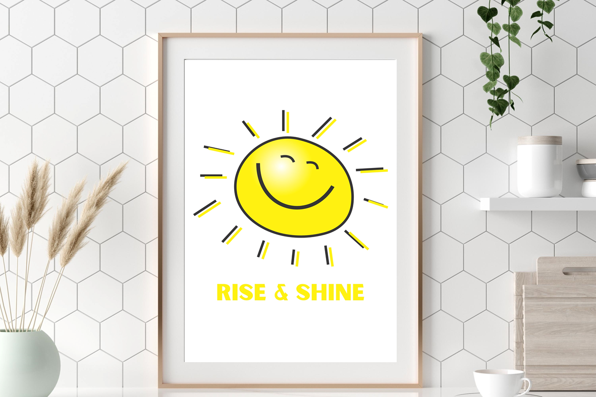 The Rise and Shine wall art print featuring a yellow smiley sun with soft sun rays and the typography “Rise and Shine”, framed in light wood and displayed above a breakfast table to add a joyful start to the day.